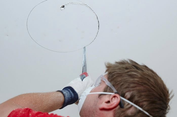 A person cutting a round hole in a ceiling using a plaster saw