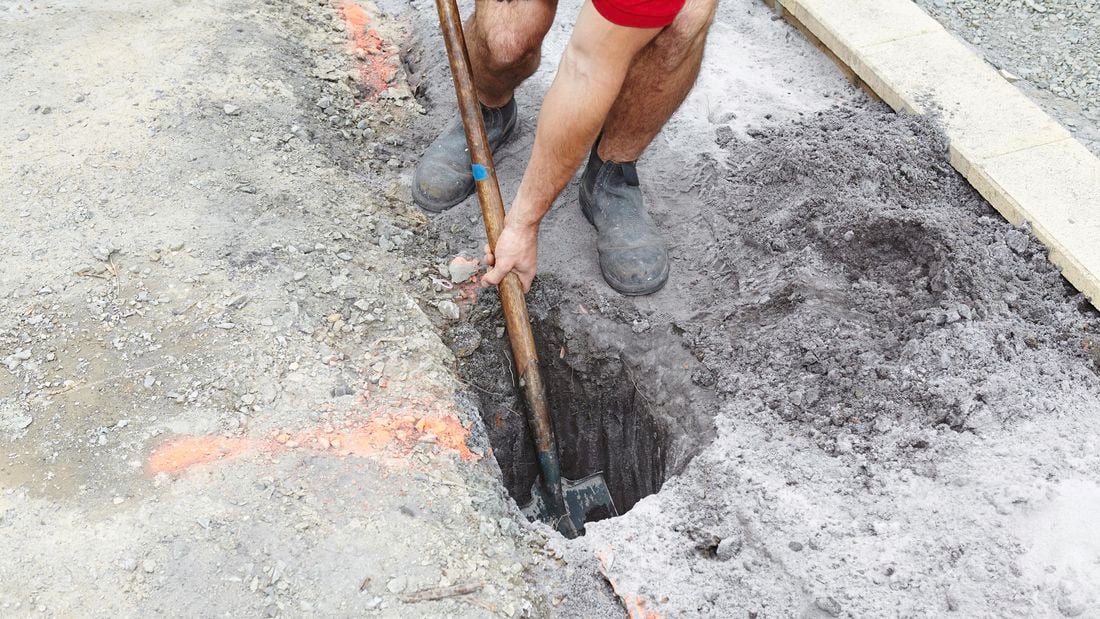 A posthole being dug out of the ground by a Bunnings team member with a shovel