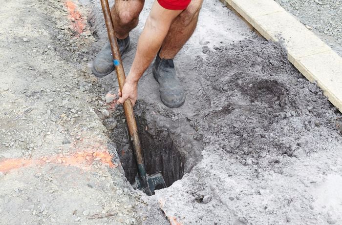 A posthole being dug out of the ground by a Bunnings team member with a shovel