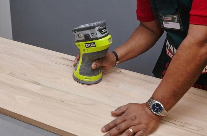 A person sanding a timber table top with orbital sander