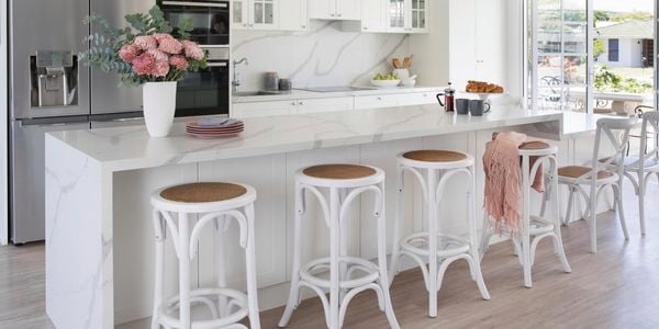 Hamptons style kitchen with white marbled benchtop and rattan textured bar stools