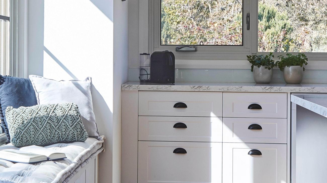 A white kitchen with some cushions by a window.