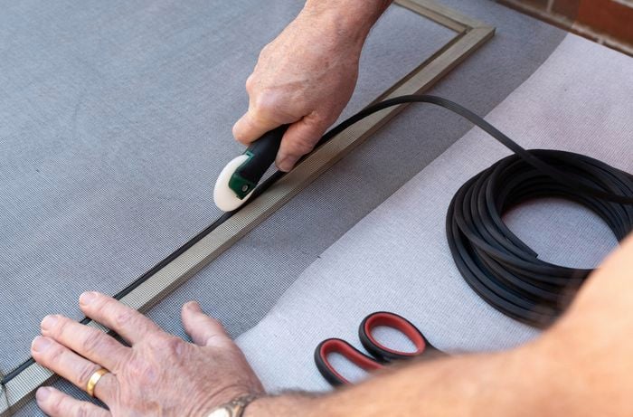 A person is using a spline roller tool to insert a spline and mesh into the groove of the frame to secure the mesh. 