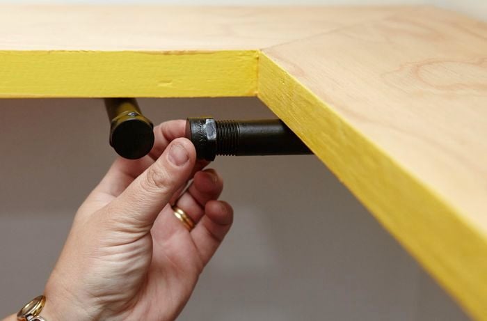 Caps being screwed onto pipes mounted to the wall as brackets for a corner shelf