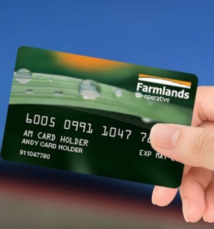 A hand holding a green farmlands credit card