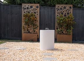 2 x screen panels against a fence and a water feature on pebbles in a backyard