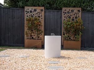 2 x screen panels against a fence and a water feature on pebbles in a backyard