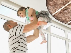 A man holding a baby and a ceiling with insulation wool.