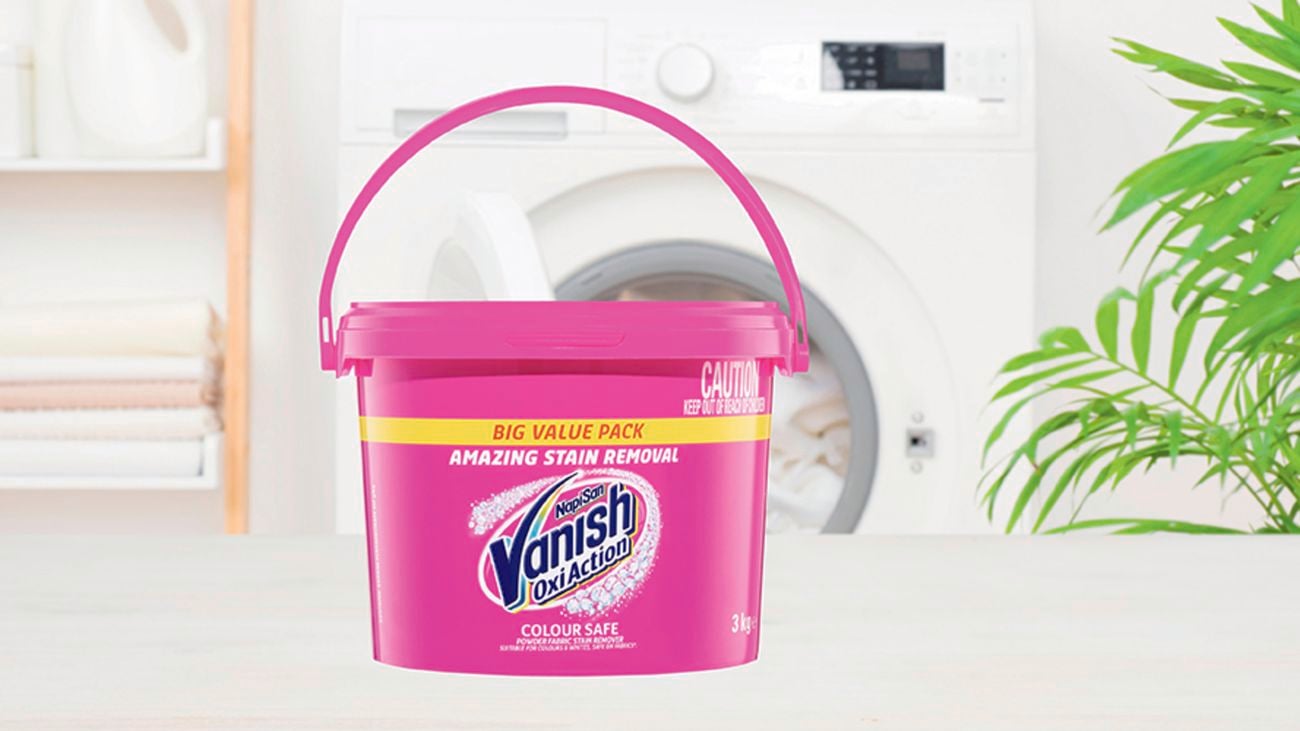 Cleaning product in pink packaging sits on bench in front of washing machine.