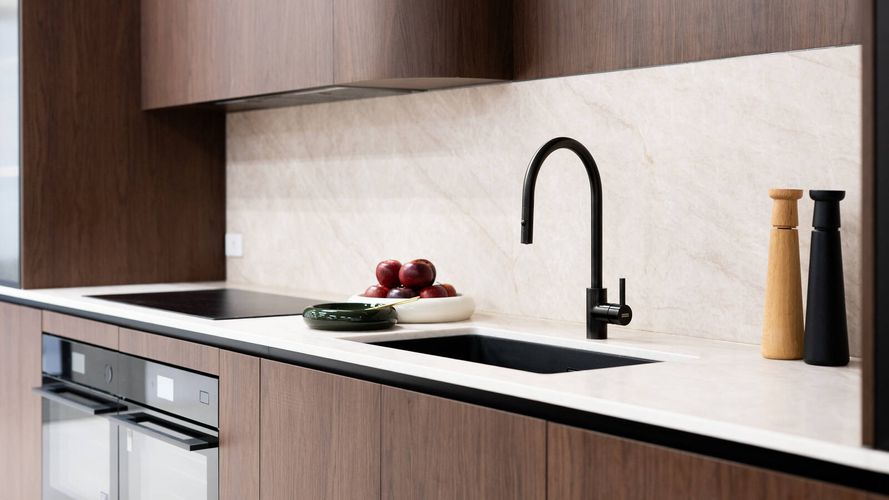 Modern kitchen with dark timber cabinetry, stone splashback, black tapware, integrated sink and built-in appliances.