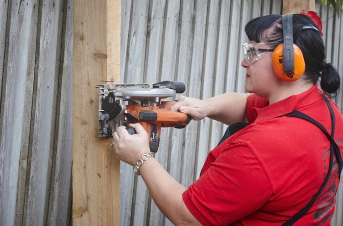A person wearing protective gear cutting into a fence post using a circular saw