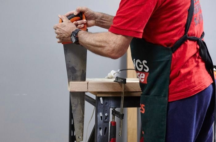 A check-out being cut into the base of a chair to make room for a back support using a handsaw