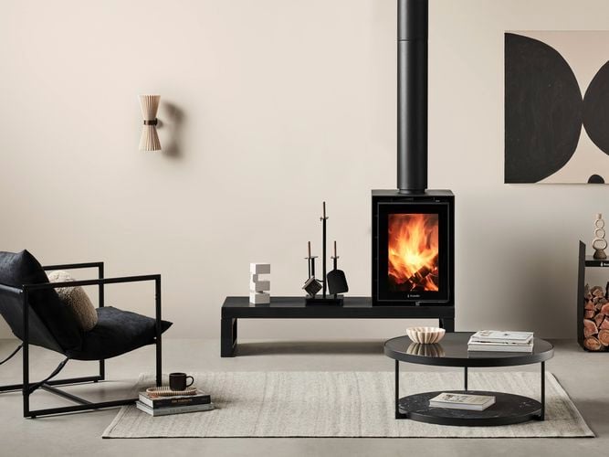A furnished lounge room with an indoor wood heater in it and carpet on the floor.