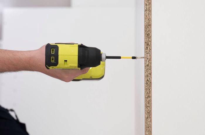 A person is using a power drill to drive a screw into the back panel of the corner base cabine