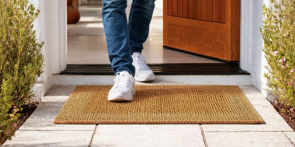 Close-up product image of a rolled doormat showing textured material and edge detail against a dark background.