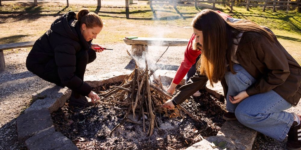 Three
  women lighting fire in firepit outside together