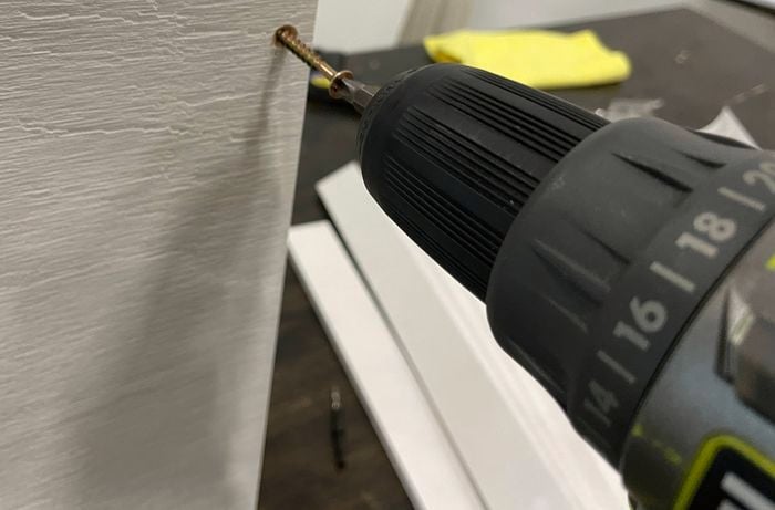 A drill is used to secure the top panel to a side panel with screws