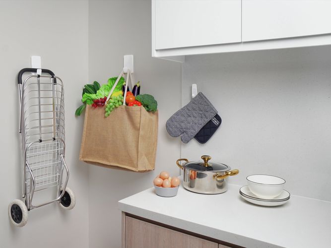 3M Command Hooks used in a kitchen to store a folding trolley, reusable grocery bag and oven mitts on the wall for easy access.