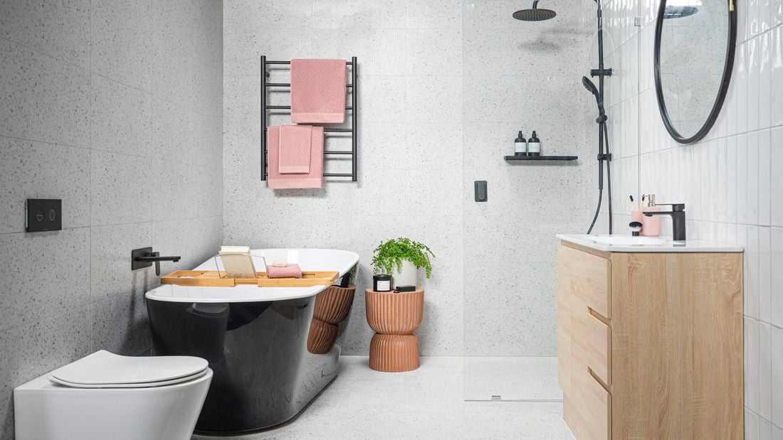 Bright bathroom with black bath tub, towel rail and tapware and terrazzo shower wall and toilet.