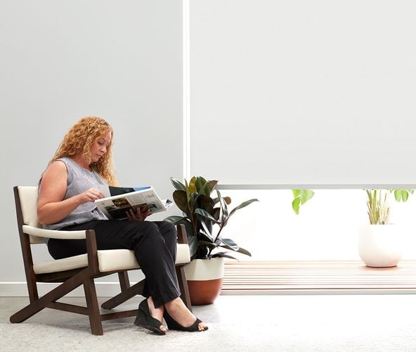 Woman sitting in an armchair in front of a window with a white roller blind