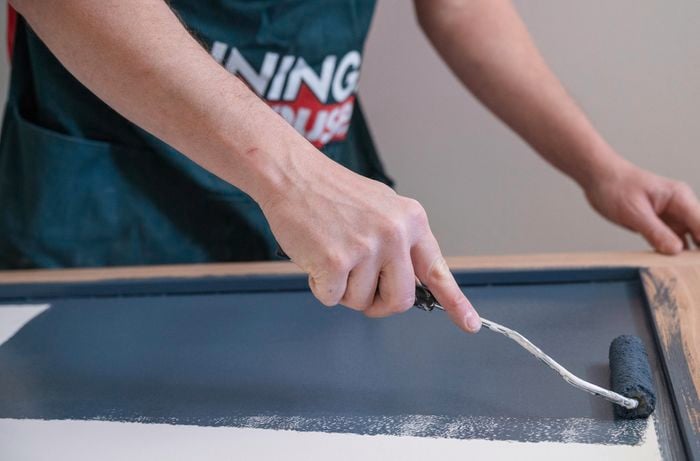 A person painting the door using enamel paint and a sponge roller.