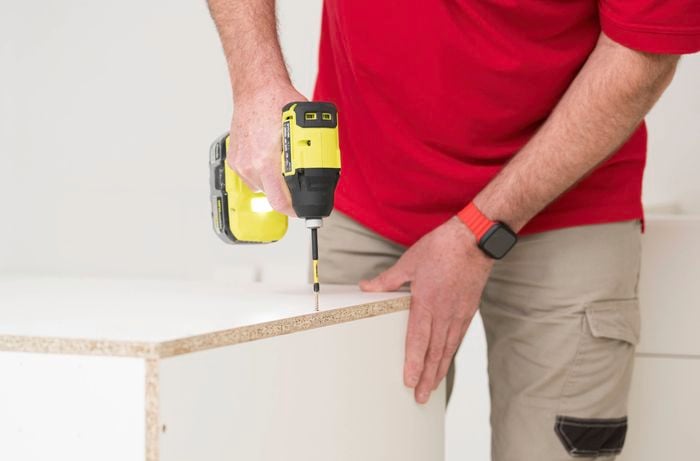 A person is using a power drill to attach the side panels in place through the pre-drilled holes.