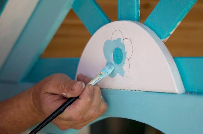 A hand holding a paintbrush to paint flower designs on the cubby house