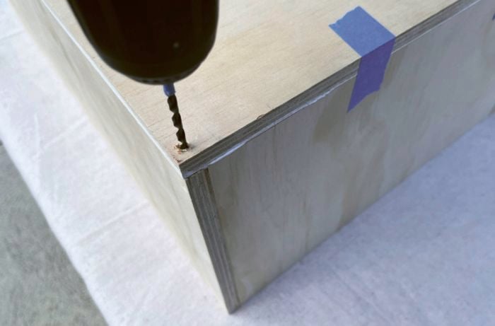 A drill bit predrilling into the corner of a wooden box.