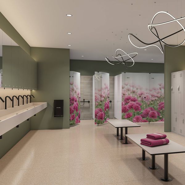 Contemporary locker room with rows of white lockers, bench seating, a long vanity with multiple taps and mirrors, and private shower cubicles decorated with floral graphics. The space features green walls, modern pendant lighting and a clean, spacious layout designed for shared use.