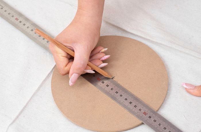 A person is using ruler and pencil to mark the centre line on a round template to draw the scallops. 