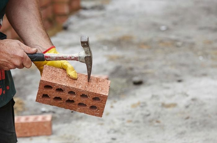 Person hitting brick with sharp edge of hammer.