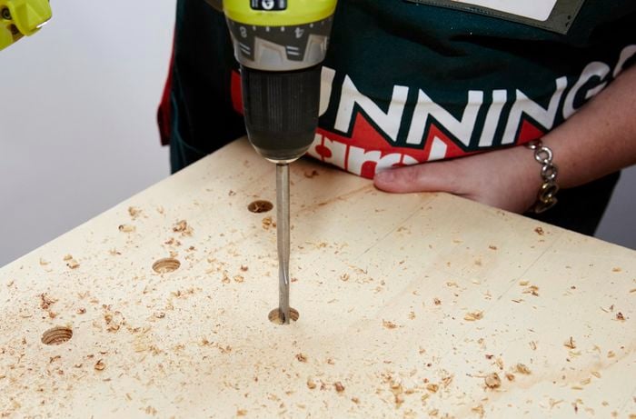 A person drilling holes in a plywood sheet using a spade bit