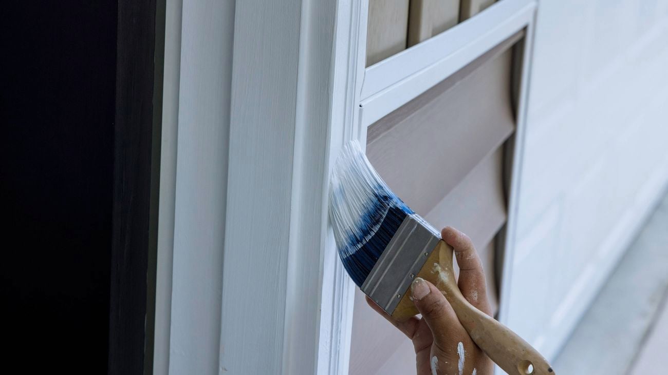 A hand painting exterior white trim with a paintbrush