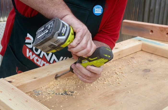 A person drilling a hole diagonally through pine timber