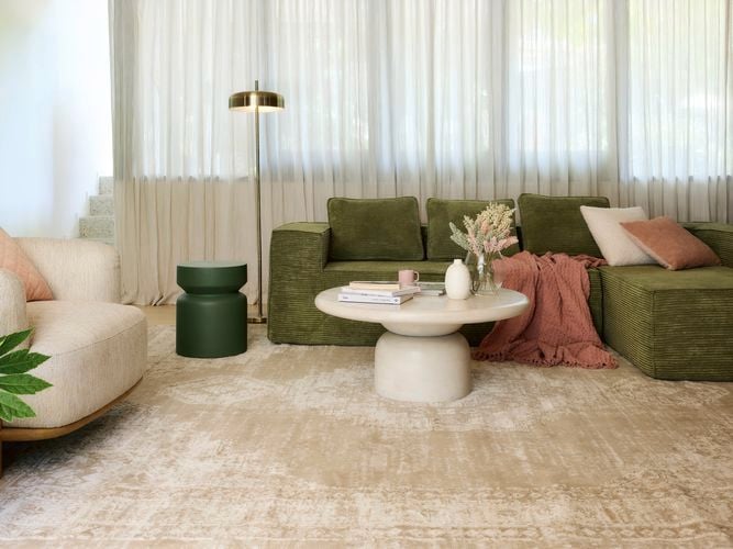 A lounge room with a green couch, white couch, coffee table and a rug on the floor.