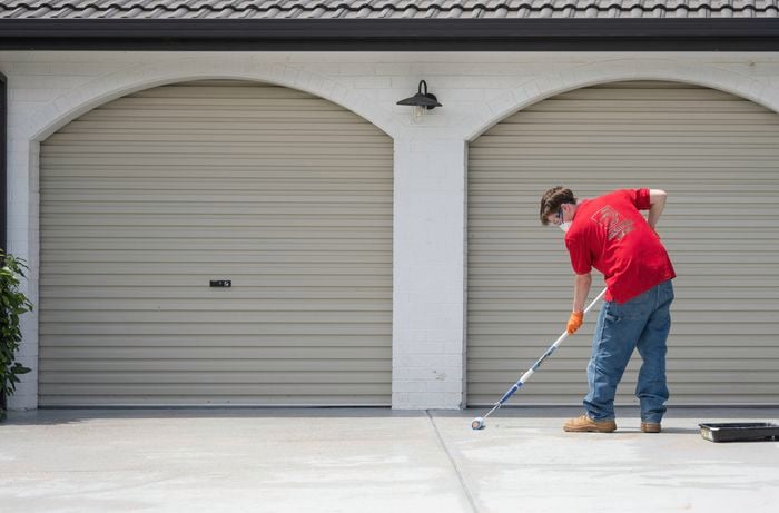 A Bunnings Team Member is applying the primer on a concrete driveway with a roller.