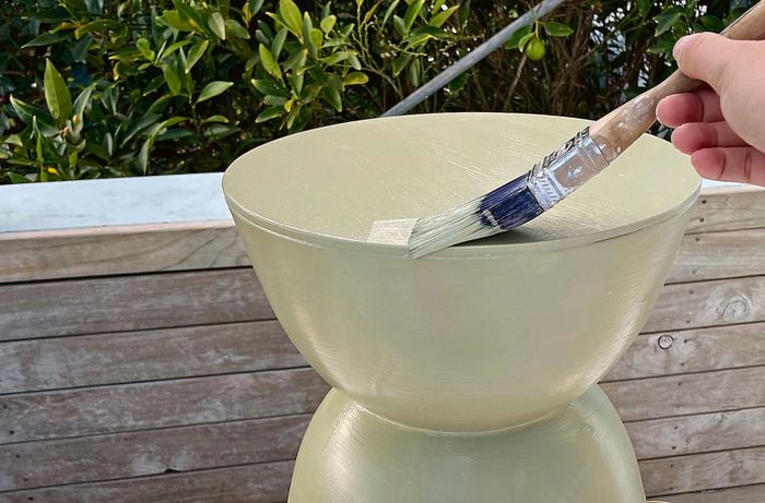 A person paints a D.I.Y. planter plinth in a light green colour