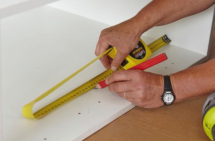 A person marking inside a cabinet using a measuring tape