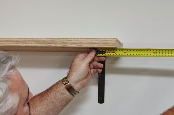 A person measuring from a bracket to the end of a shelf