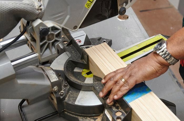 A person positioning pine timber under a drop saw