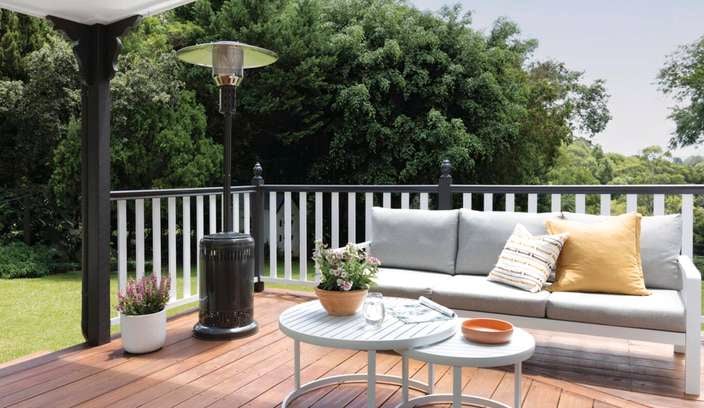 Outdoor entertaining area with wooden deck, grey and white lounge and coffee table, and an outdoor heater.