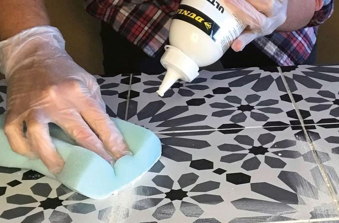 Two hands applying grout to tiles