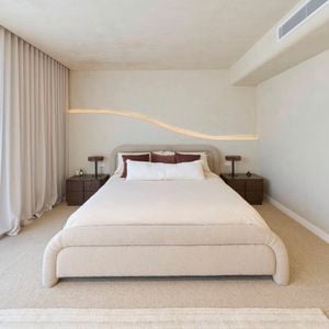 A furnished bedroom, with a be, two side tables, another table with a vase with flowers on it and carpet in the room.