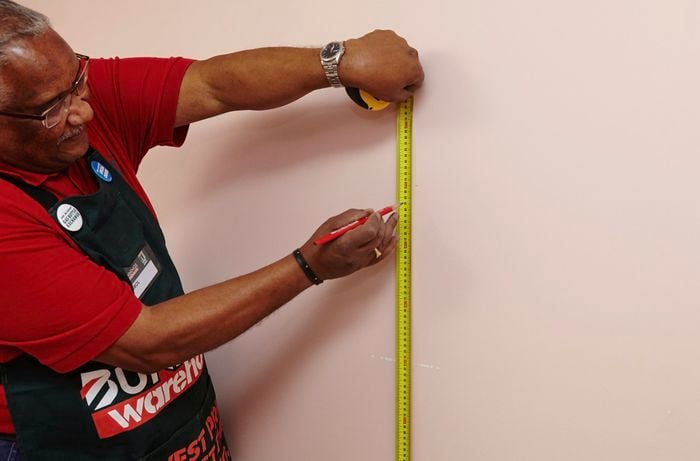 A person marking a measurement on a wall using a measuring tape 