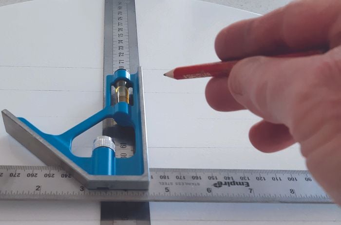 Hand uses pencil and combination square ruler to make markings on table
