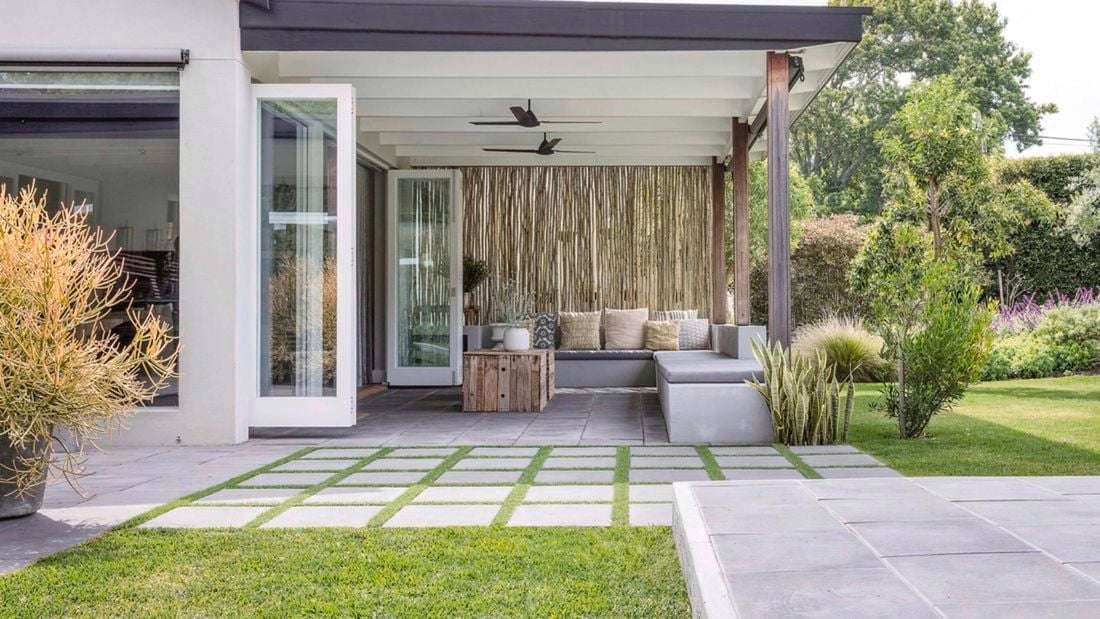 Covered outdoor patio with modern seating, ceiling fans, stepping stone pavers and landscaped lawn.