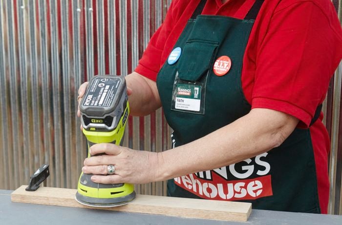 A person sanding timber with an orbital sander