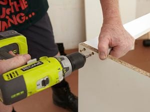 Person using a cordless driver to attach two cabinet panels