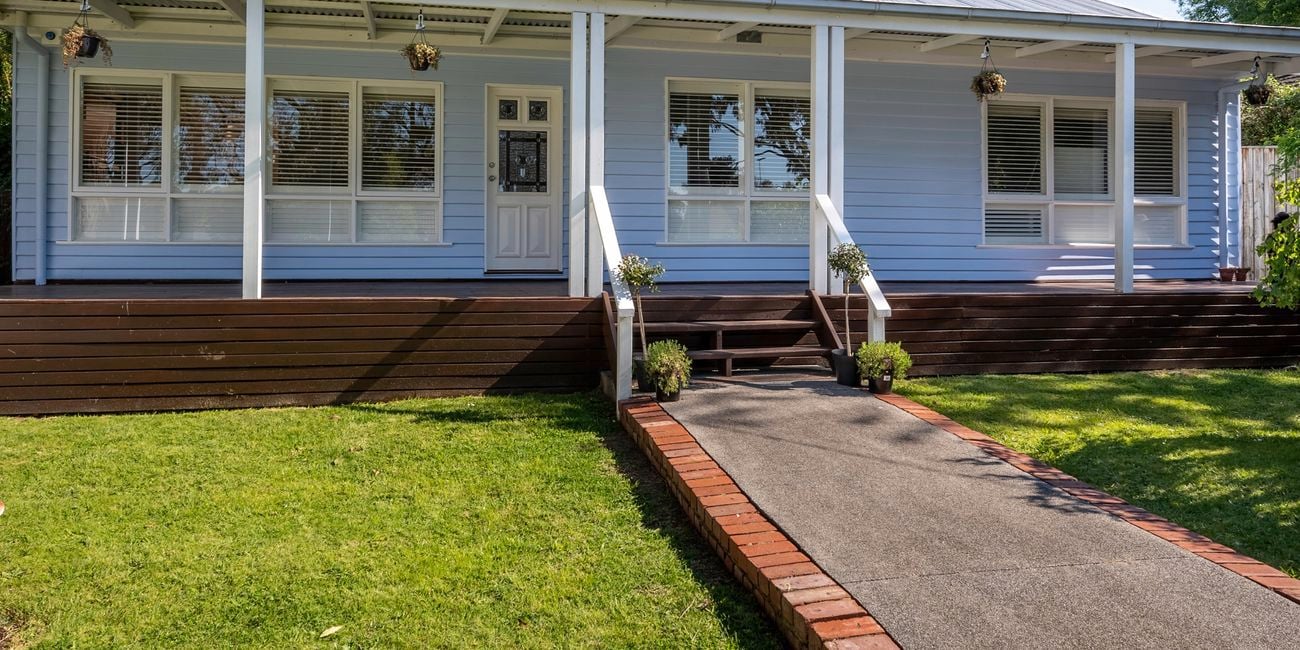 Front yard with big grass patch, paved path and a grey weatherboard house.