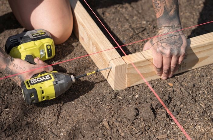 A person is using a Ryobi power drill to fasten two timber pieces together following the string line as a guide.